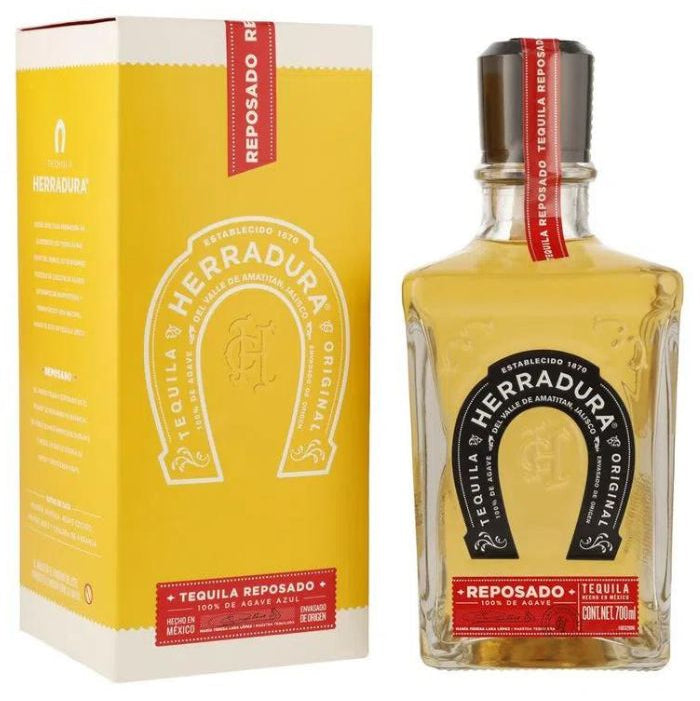 Caja de color amarillo y sellos rojos, junto a una botella de tequila Herradura Reposado de 700 ml. 